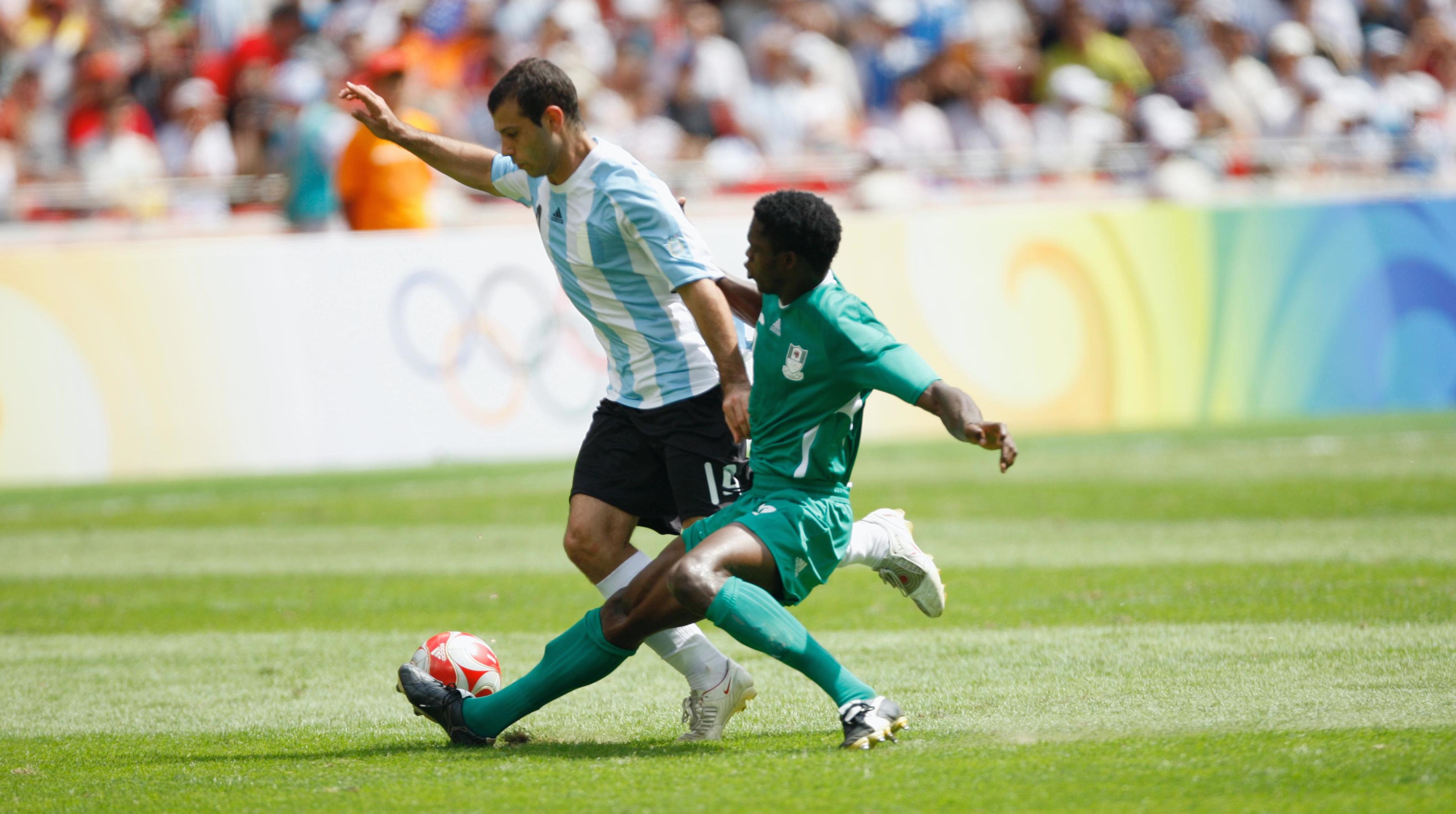 Two fotballplayers on the field in a match. One player tries to tackle the ball from the other player