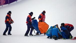 Several medical personell walking on snow over to an athlete that have fallen.