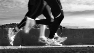 Black and white photo of the legs of some athletes running outside.
