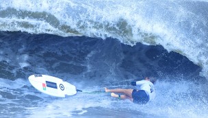 Athlete in the water, surfboard on the left, while athlete has fallen off and are landing in the water, sideways.